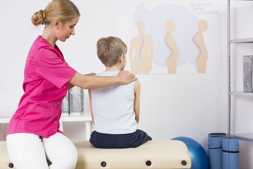 A Young Boy Is Sitting On A Table While A Nurse Examines His Back — Southern Districts Physiotherapy & Sports Injuries Clinic In Tullimbar, NSW