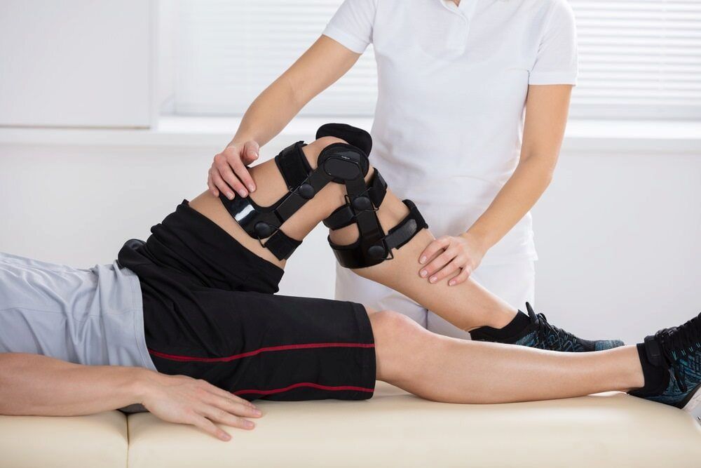 A Woman Is Helping A Man With A Knee Brace — Southern Districts Physiotherapy & Sports Injuries Clinic In Albion Park, NSW