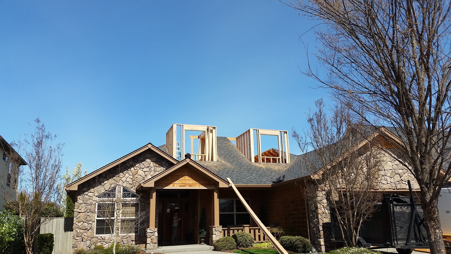 House under construction with wood framing, stone exterior, and blue sky.