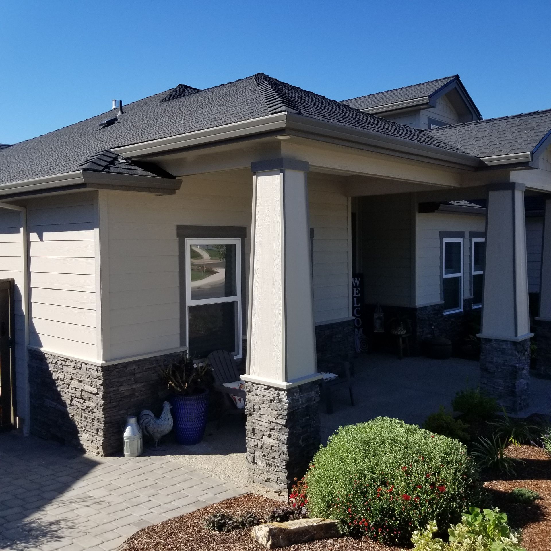 House exterior with stone accents, porch, columns, and landscaping under a clear blue sky.