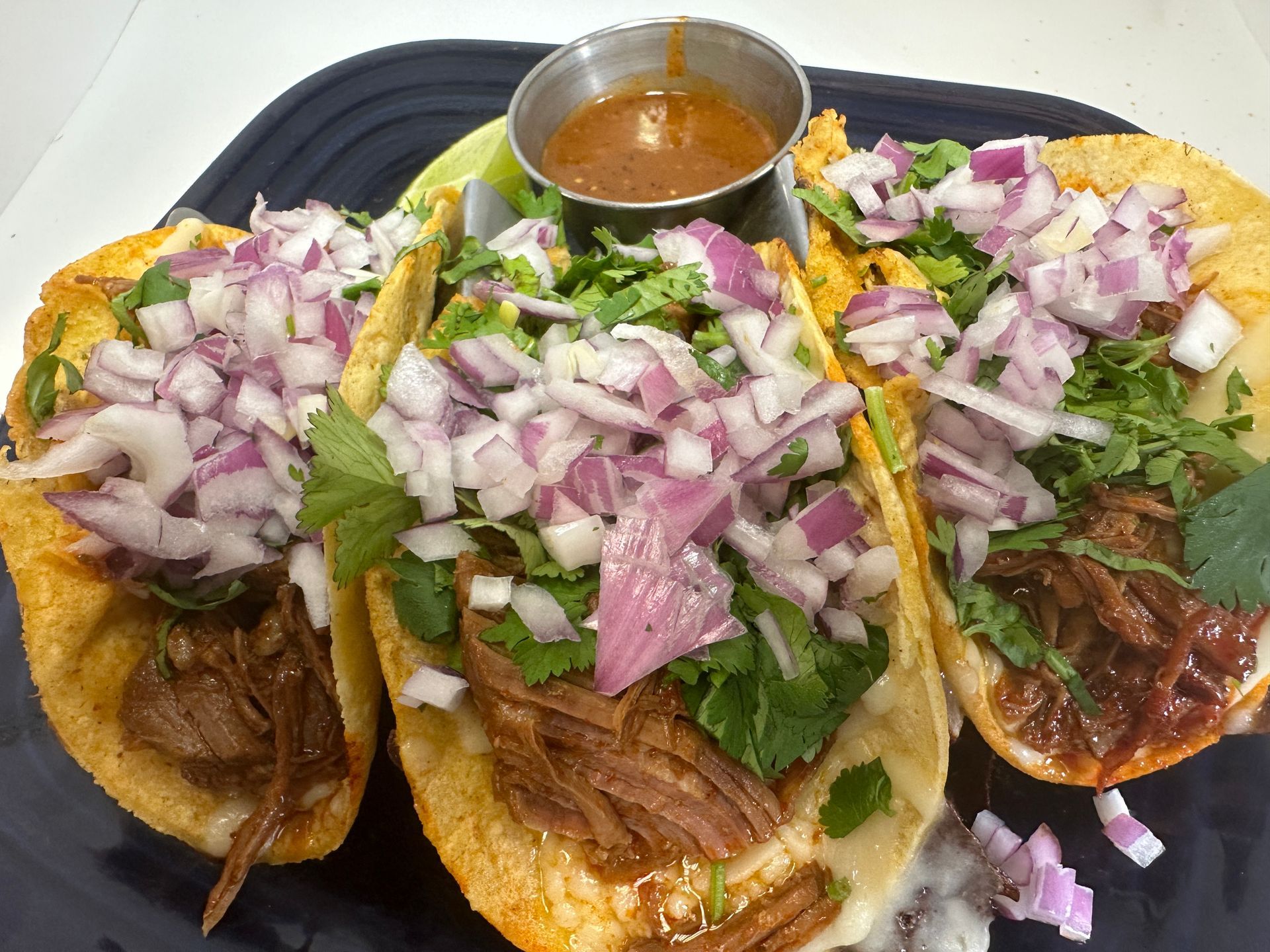 Three tacos topped with red onion and cilantro, served with salsa and lime on a blue plate.