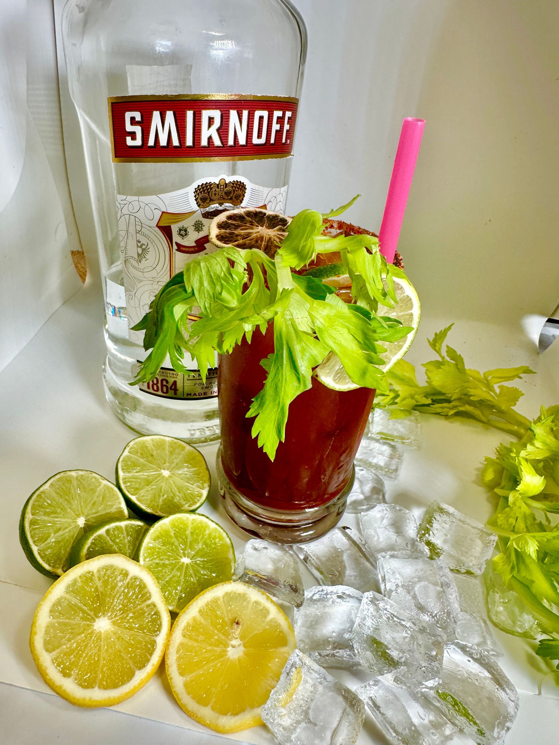 Bloody Mary cocktail with Smirnoff vodka bottle, celery, lemon/lime slices, ice, pink straw.