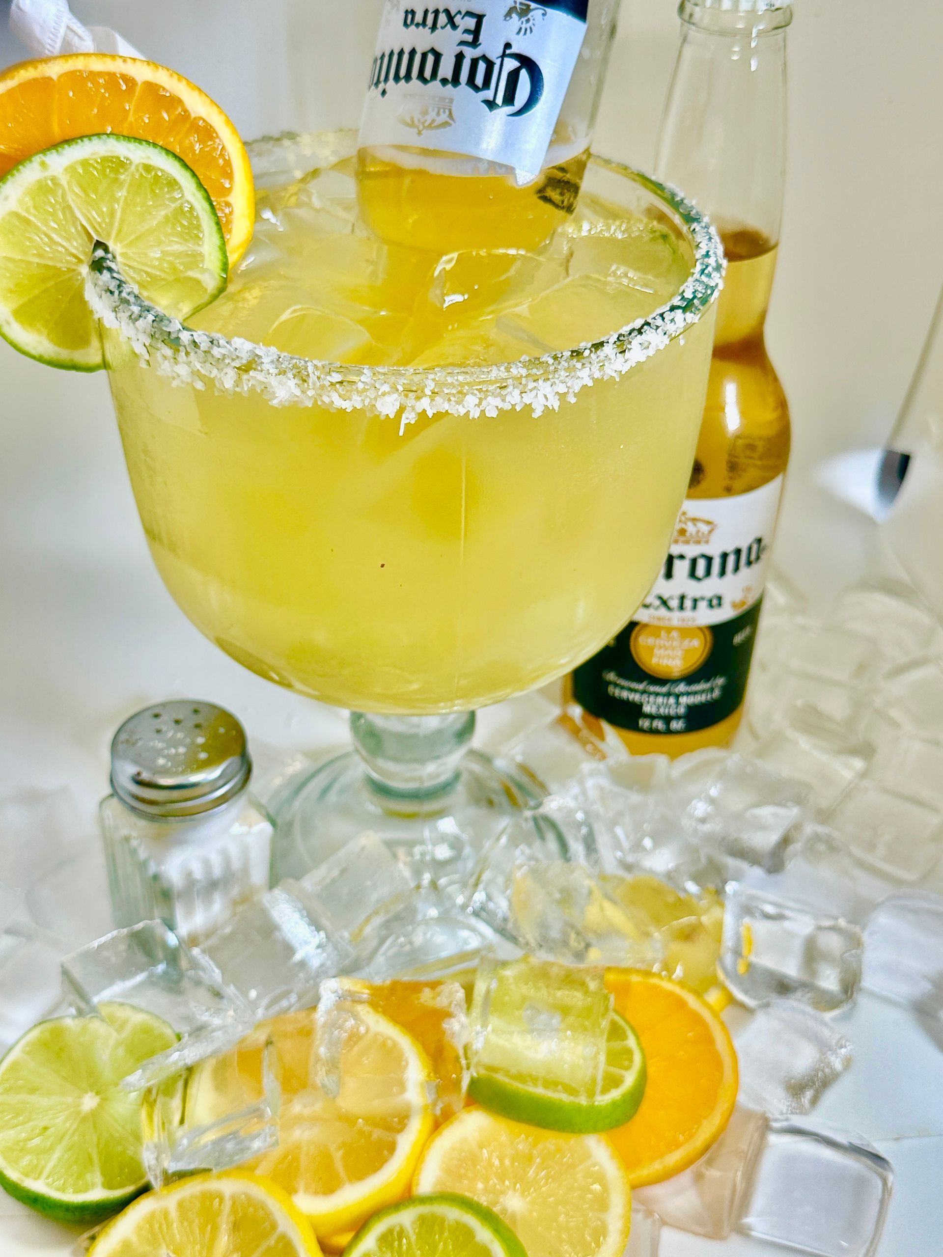 Margarita in large glass with salt rim, Corona beer, orange and lime slices.