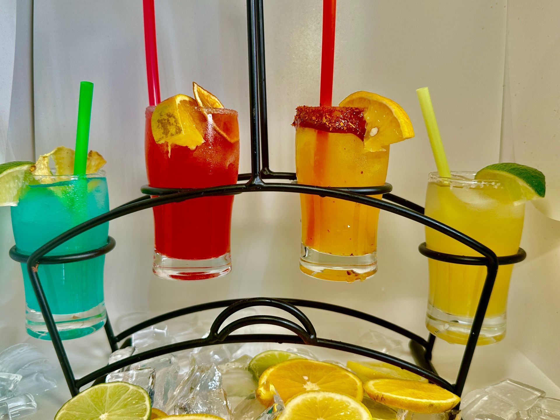 Cocktails in colorful drinks, with fruit garnishes and straws, held in a tiered rack with ice and sliced citrus.