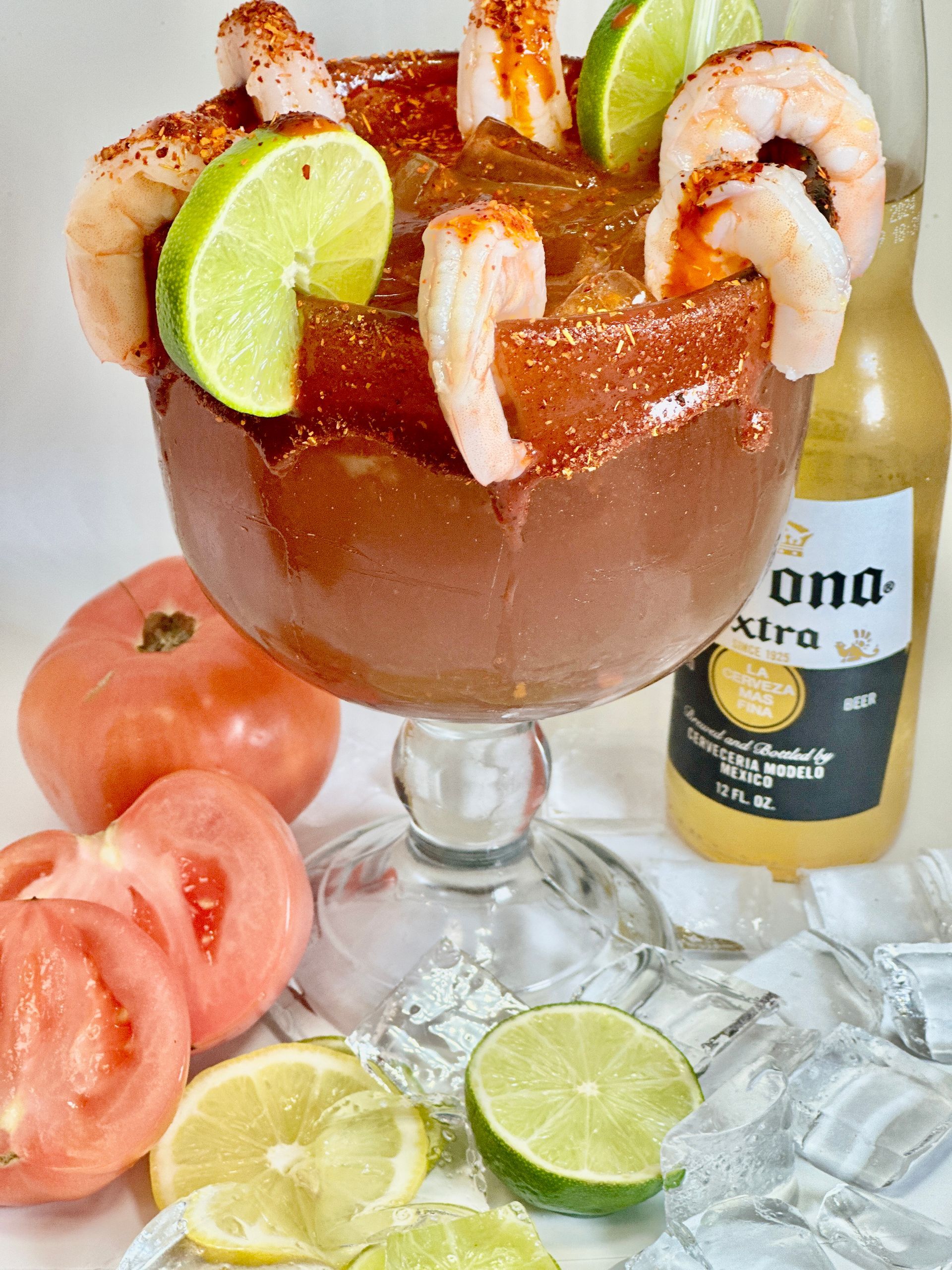 Shrimp cocktail in a glass with lime, tomato, beer bottle, and ice.