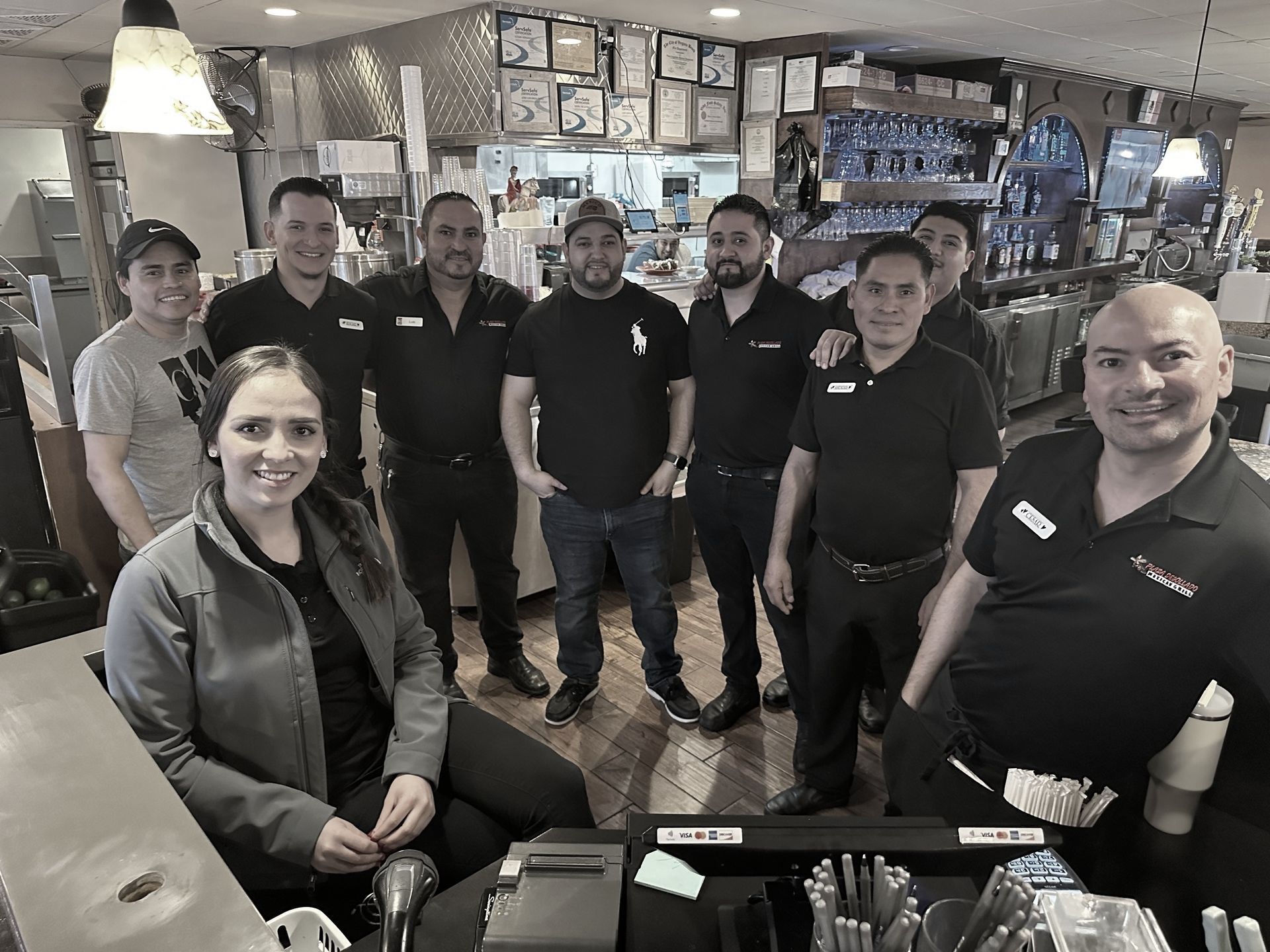 Restaurant staff posing for a photo. People in black shirts and a jacket, standing and smiling in a restaurant setting.