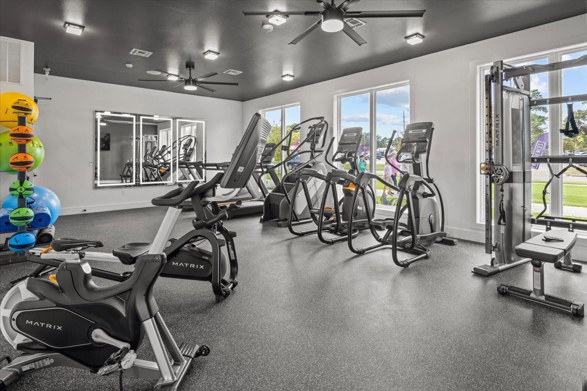 Gym interior with exercise equipment: treadmills, bikes, weight machine, mirrors, and ceiling fans.