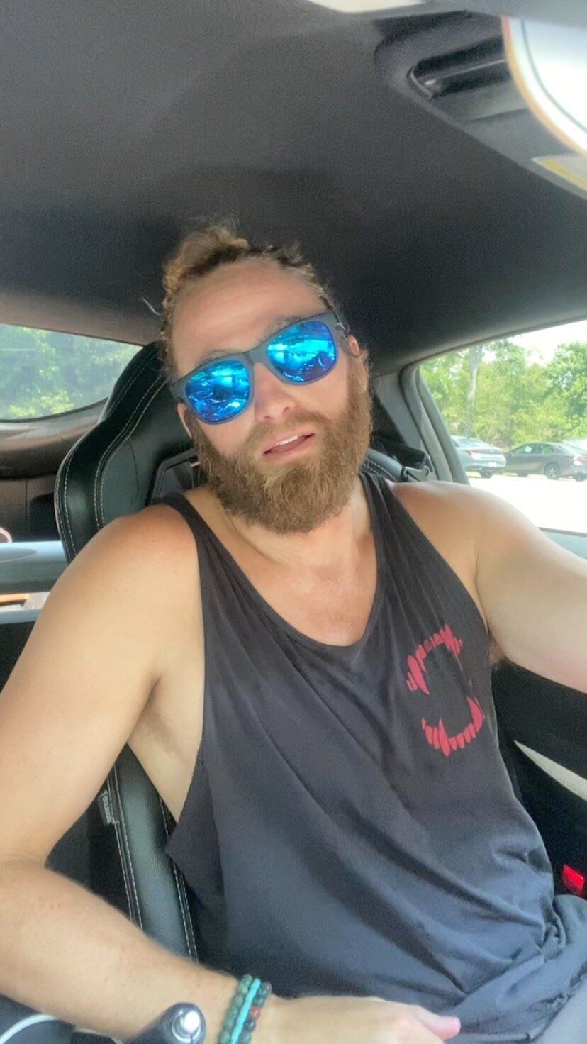 A man with a beard and sunglasses is sitting in a car.