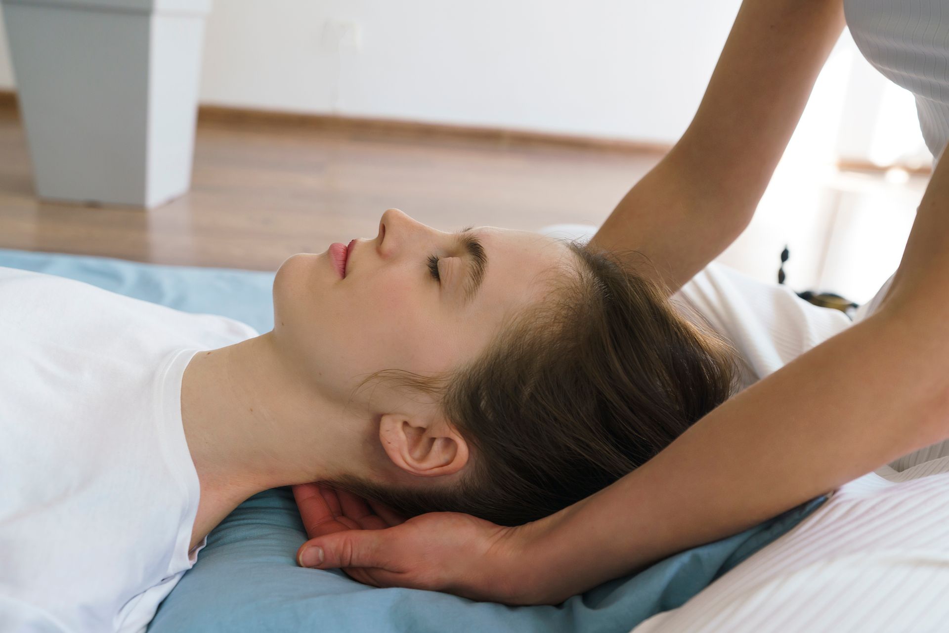 Person receiving a neck massage, eyes closed, on a blue mat. Another person's hands cradle their head.