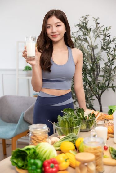 Woman in workout clothes holding a glass of liquid, surrounded by vegetables and healthy food. Woman in workout clothes holding a glass of liquid, surrounded by vegetables and healthy food.