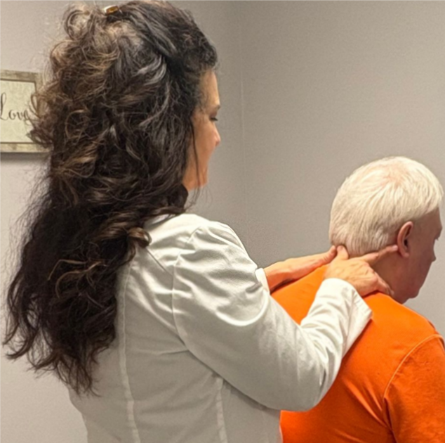 Woman in yellow top has arm stretched by therapist in a treatment room.