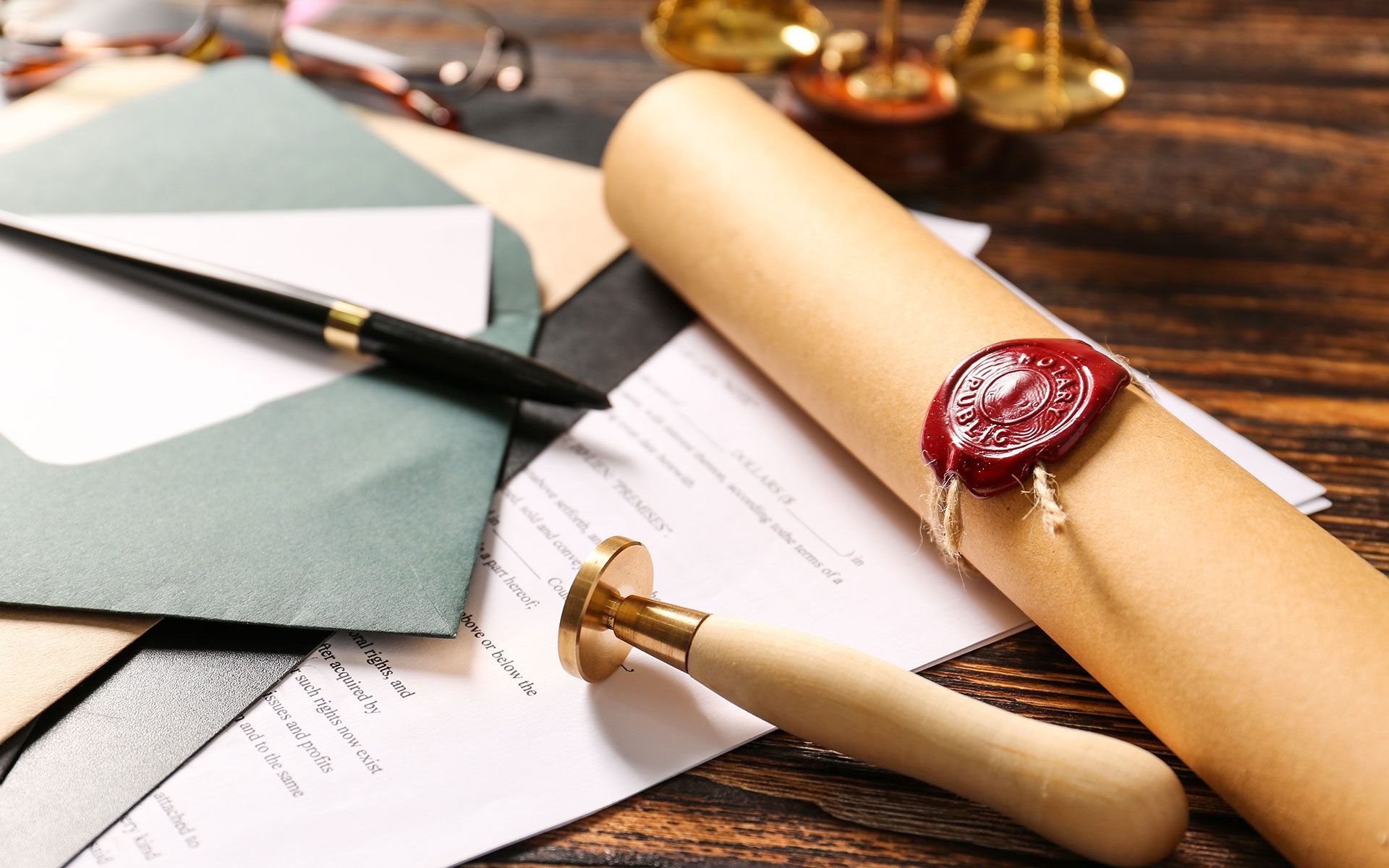 Legal documents with a scroll sealed with wax, a stamp, and a pen on a wooden surface.