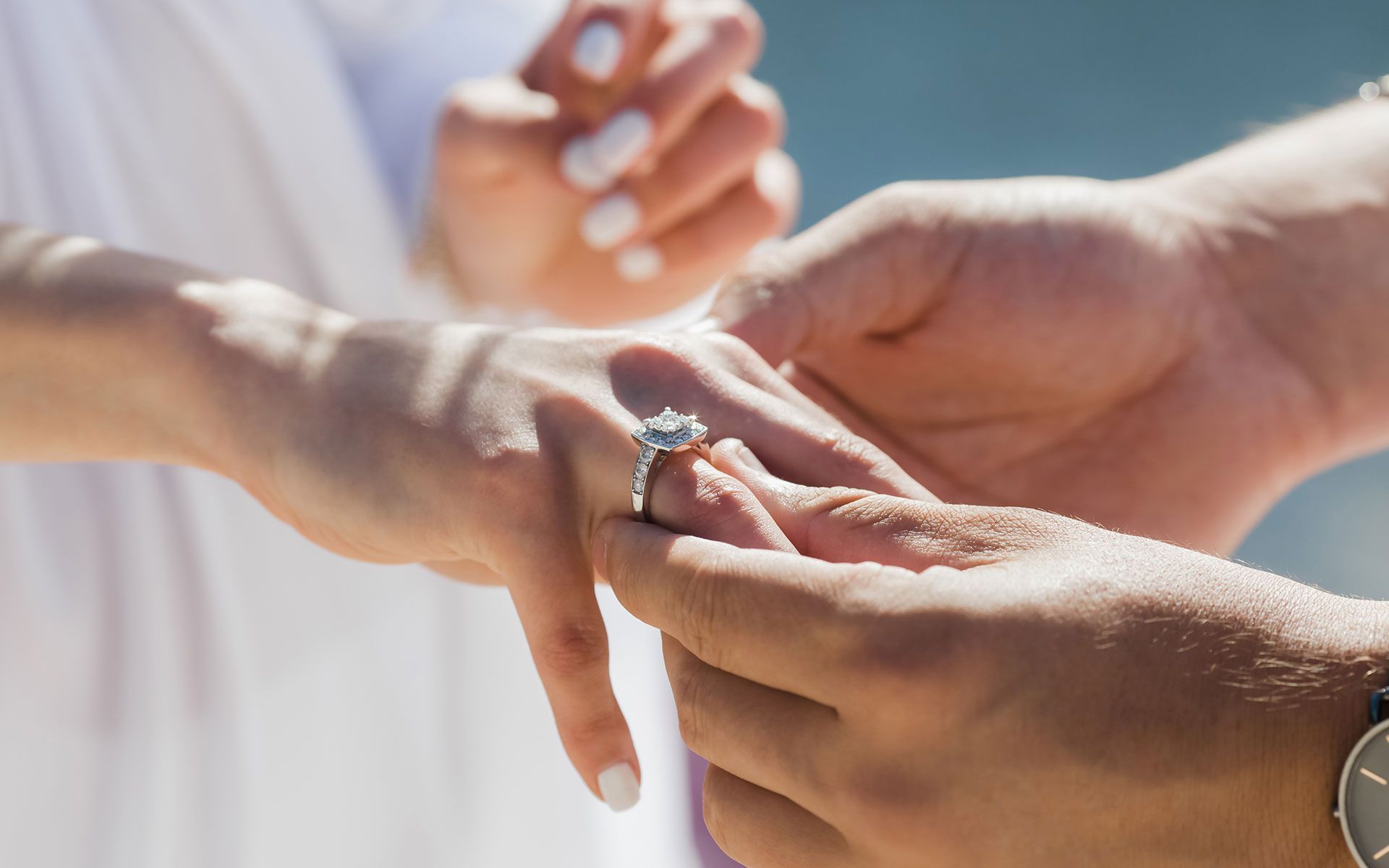 A person's hand being adorned with a diamond engagement ring by another person.