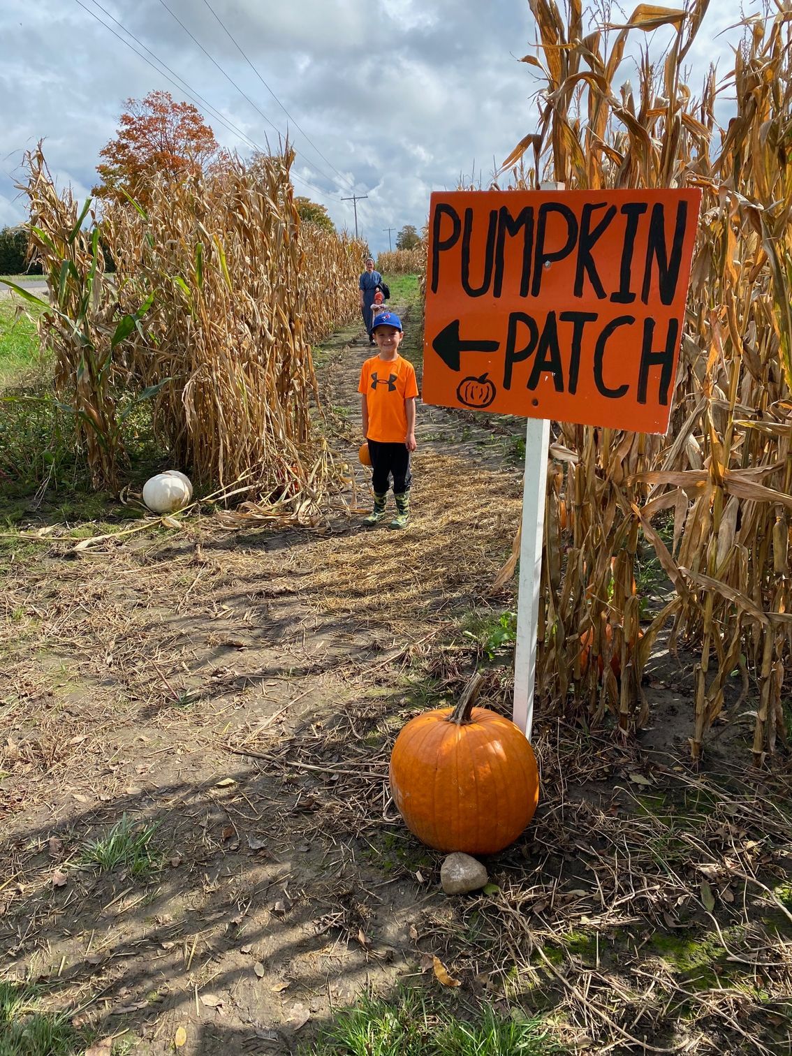 A boy is standing in front of a pumpkin patch sign.