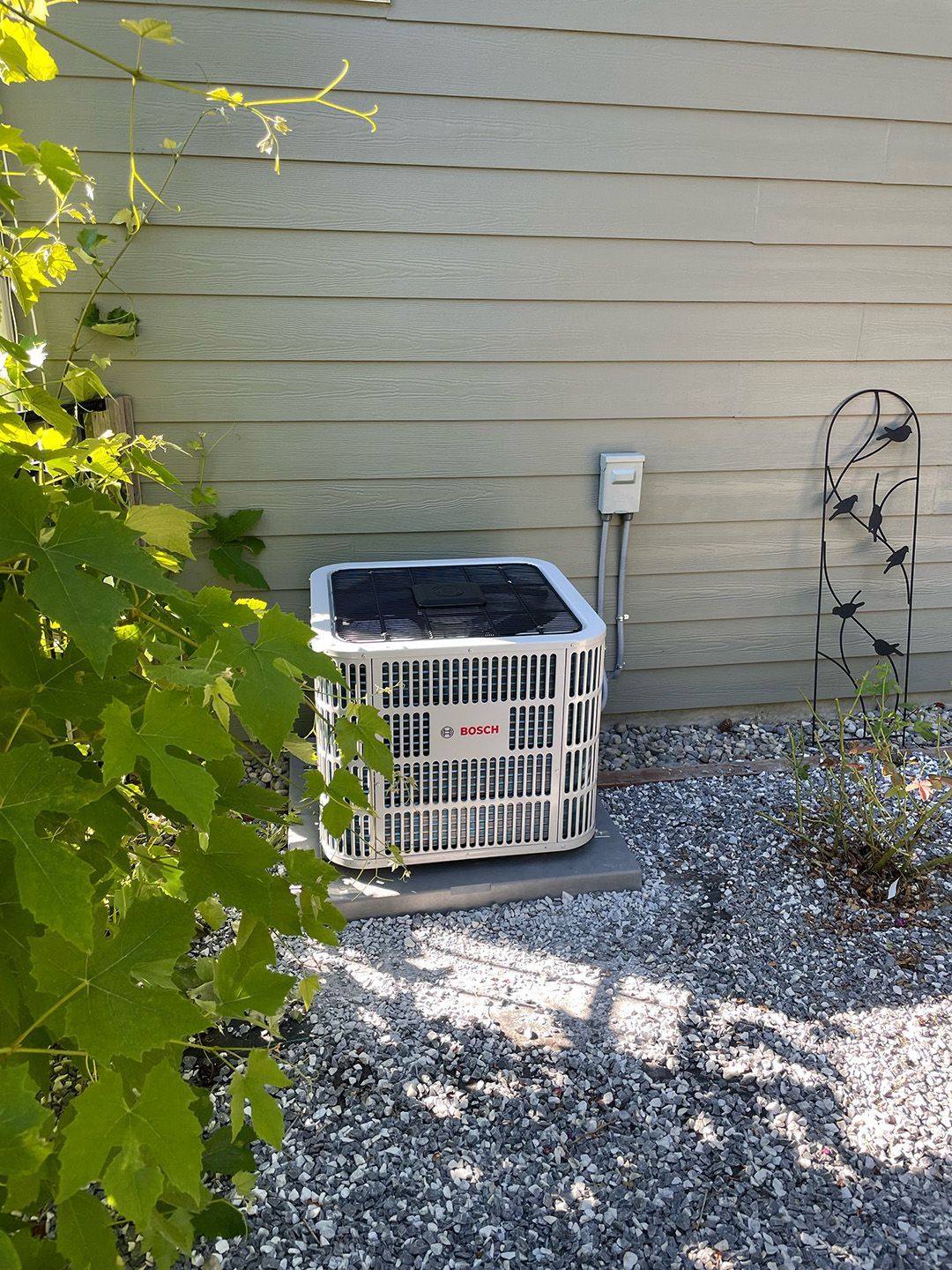 An air conditioner is sitting outside of a house next to a tree.