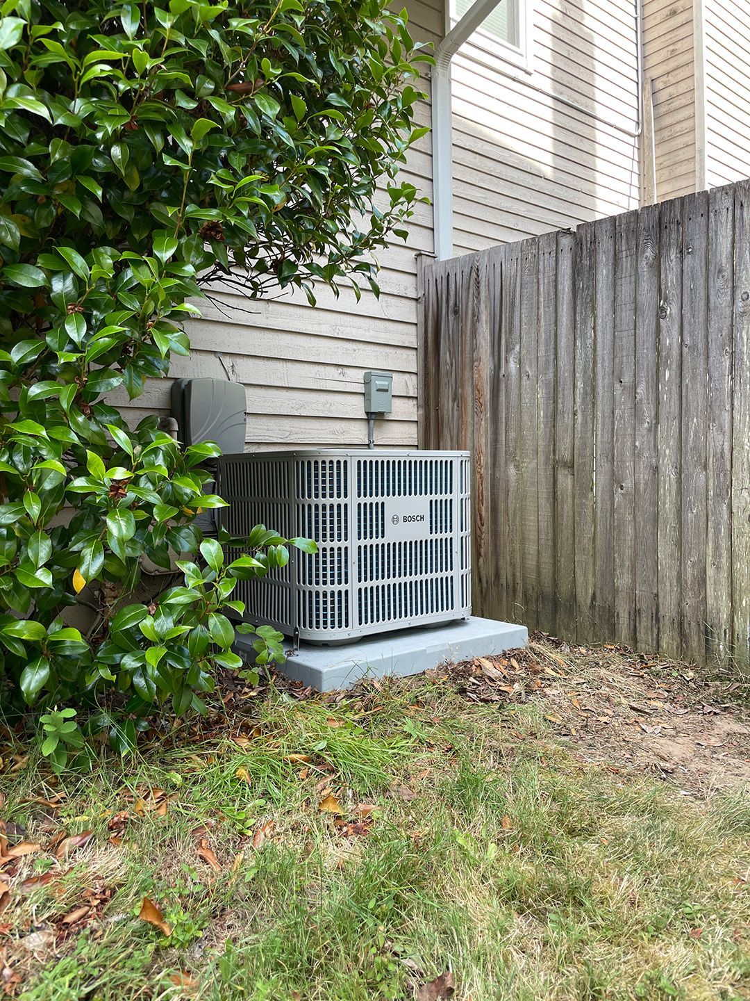 An air conditioner is sitting on the side of a house next to a wooden fence.