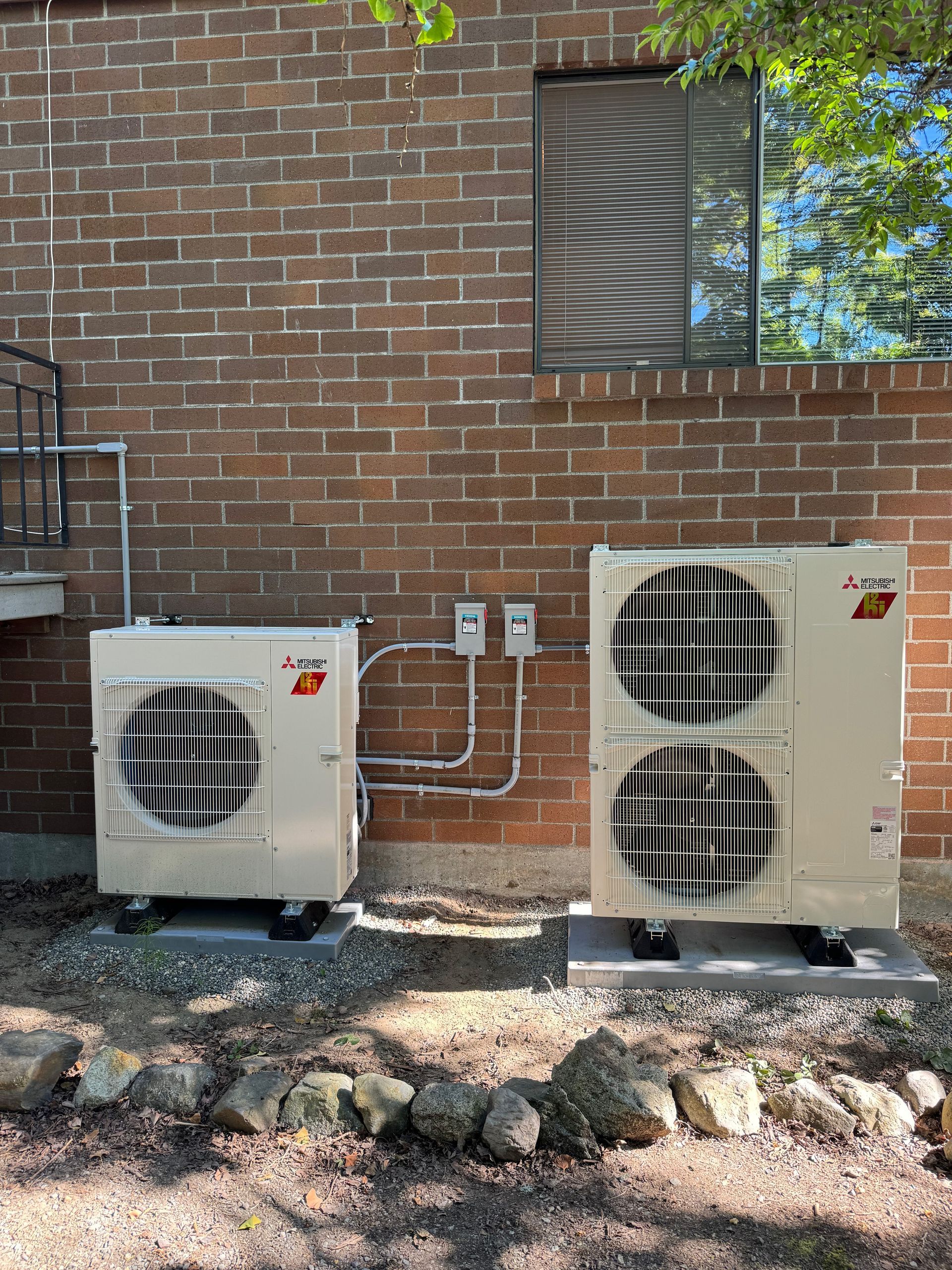 Two air conditioners are sitting outside of a brick building installed by Ready Energy Solutions.