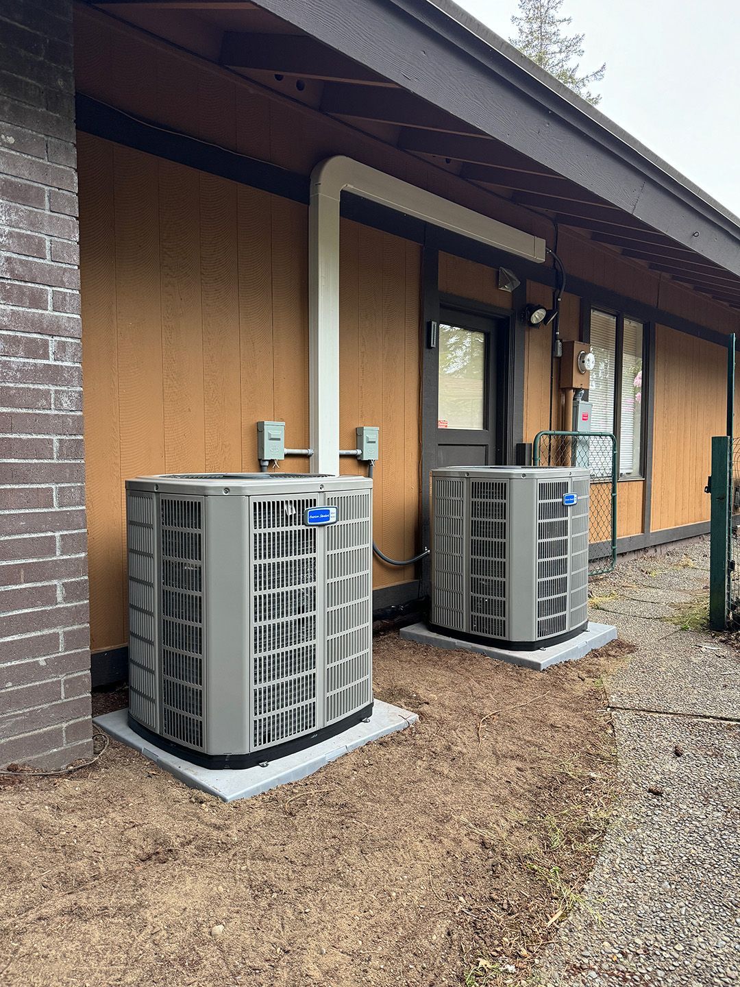 Two air conditioners are sitting on the side of a building installed by Ready Energy Solutions.