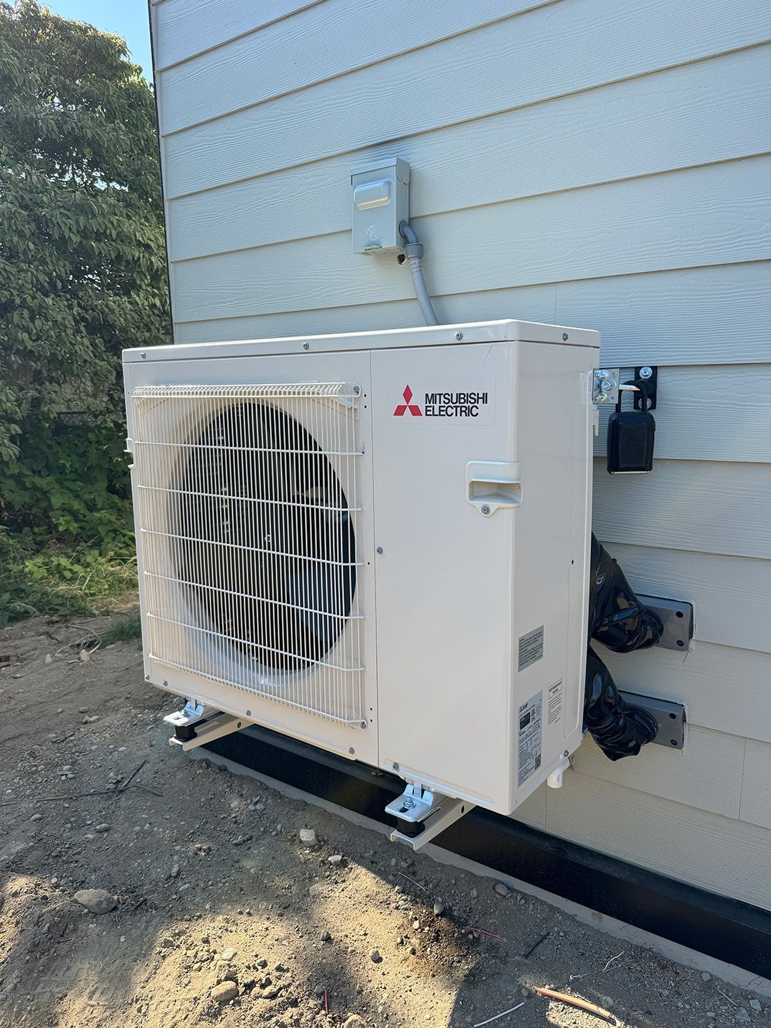 A white air conditioner is sitting on the side of a house installed by Ready Energy Solutions.