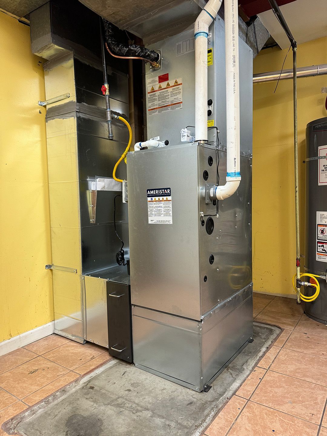 A large air conditioner is sitting in a room next to a water heater installed by Ready Energy Solutions.
