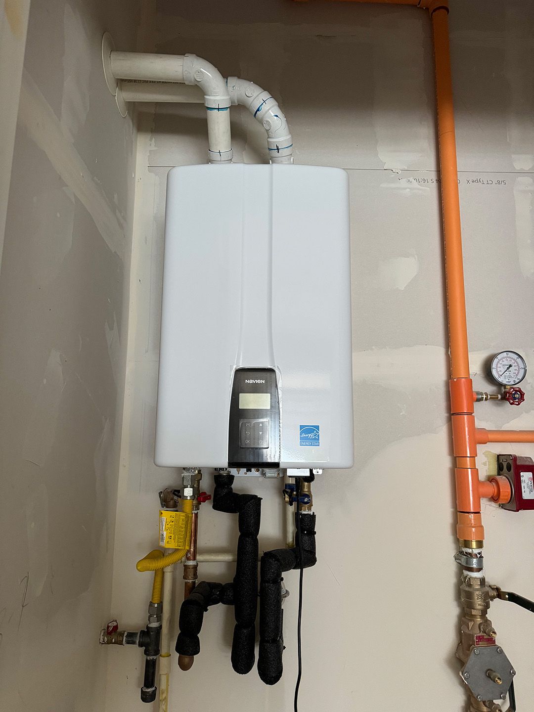 A white water heater is hanging on a wall next to pipes installed by Ready Energy Solutions.