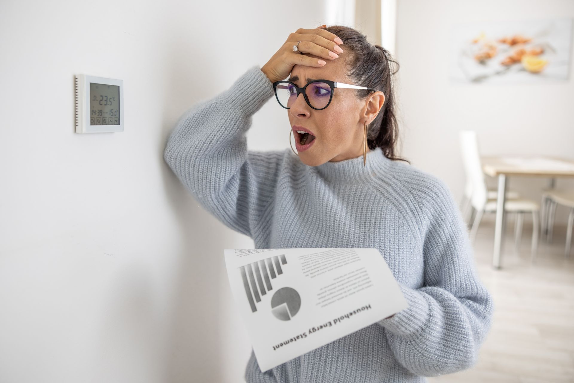 Homeowner reviewing a high summer energy bill while adjusting a thermostat to improve HVAC.