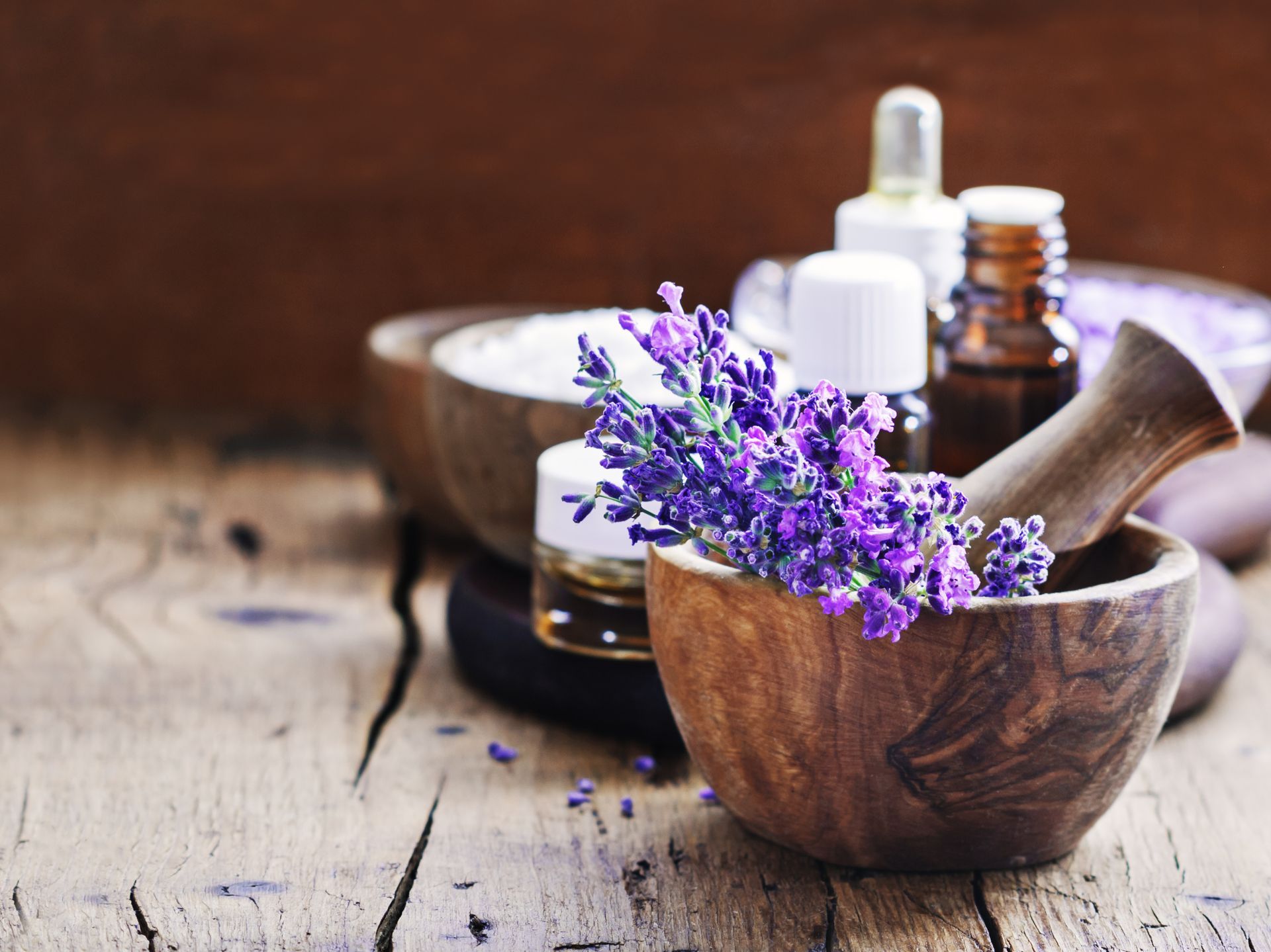 Lavender sprigs in a wooden mortar, essential oil bottles, and bath salts on a rustic wooden surface.