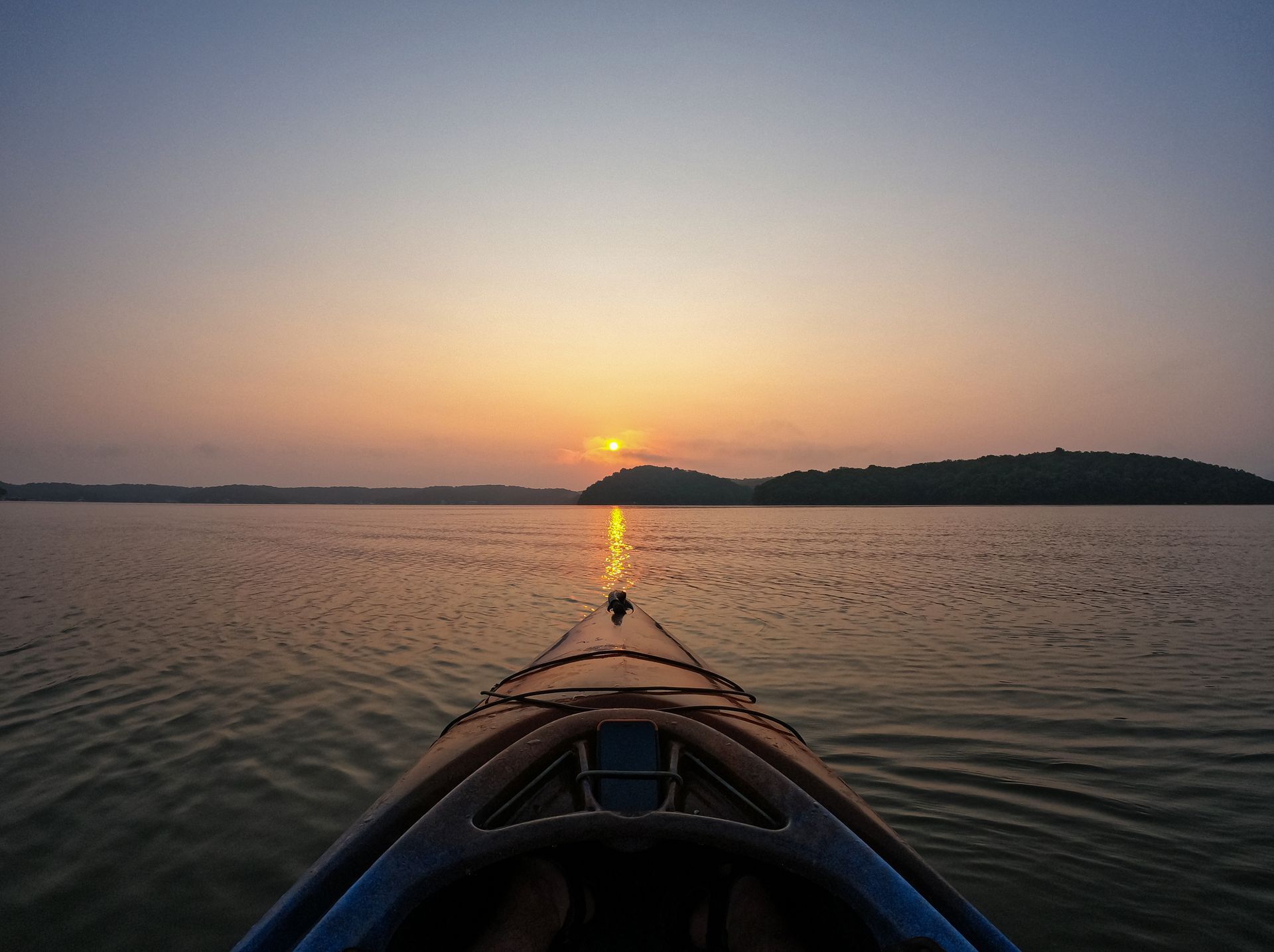 Kayaking on calm water at sunset, with the sun low on the horizon.