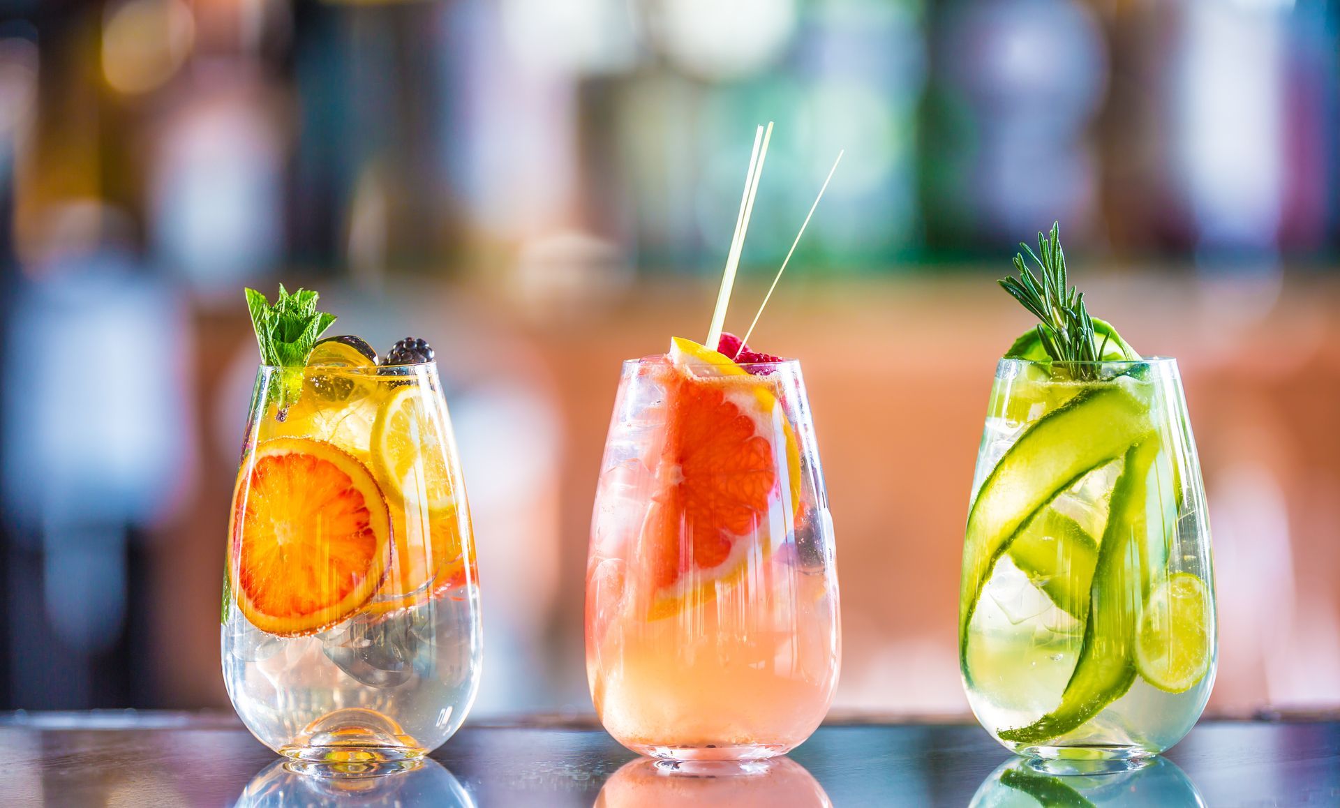 Three colorful cocktails with fruit and garnishes on a bar.