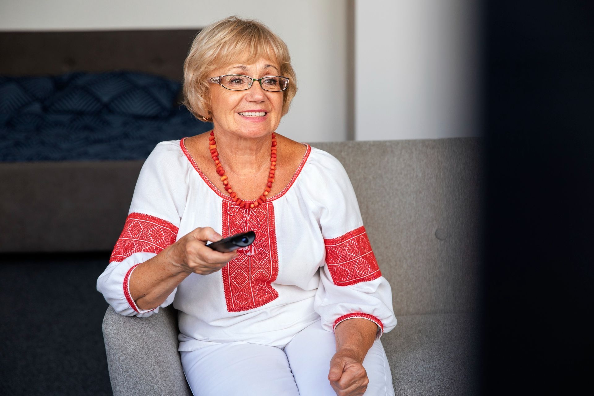 En man der sidder på en blå sofa og har en fjernbetjening i hånden