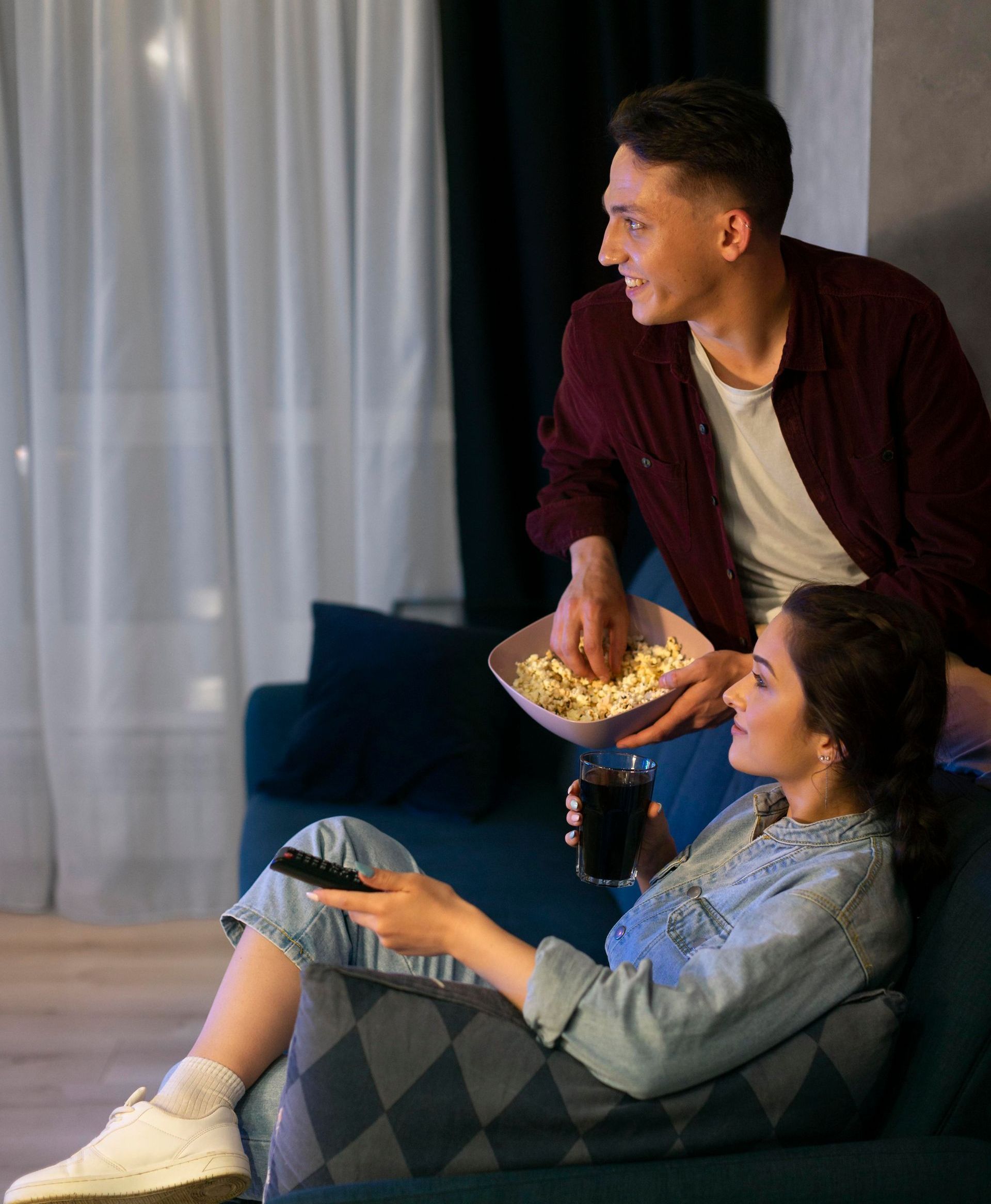 En mand holder en skål popcorn ved siden af en kvinde, der sidder i en sofa.