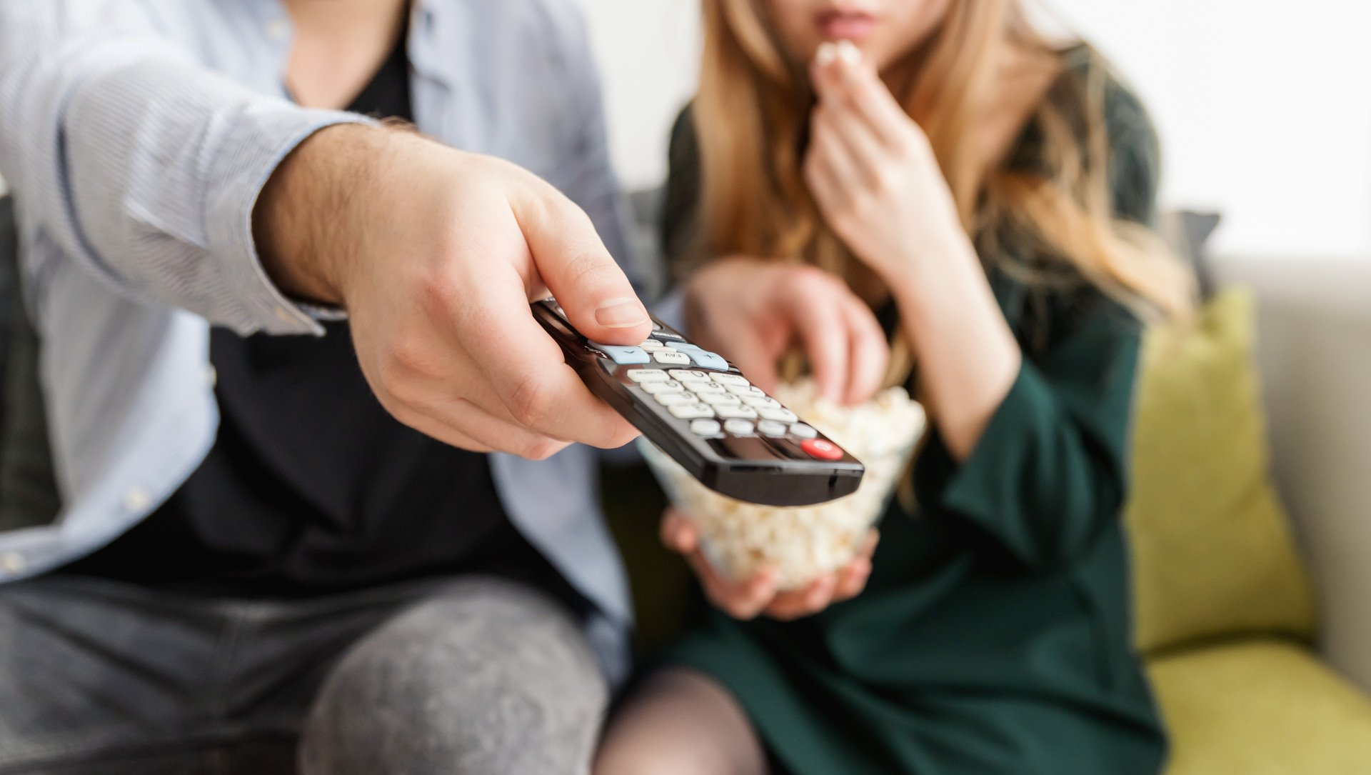 En mand holder en fjernbetjening, mens en kvinde spiser popcorn.