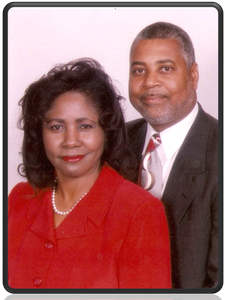 Couple, woman in red blazer, man in suit and tie, smiling, studio setting.