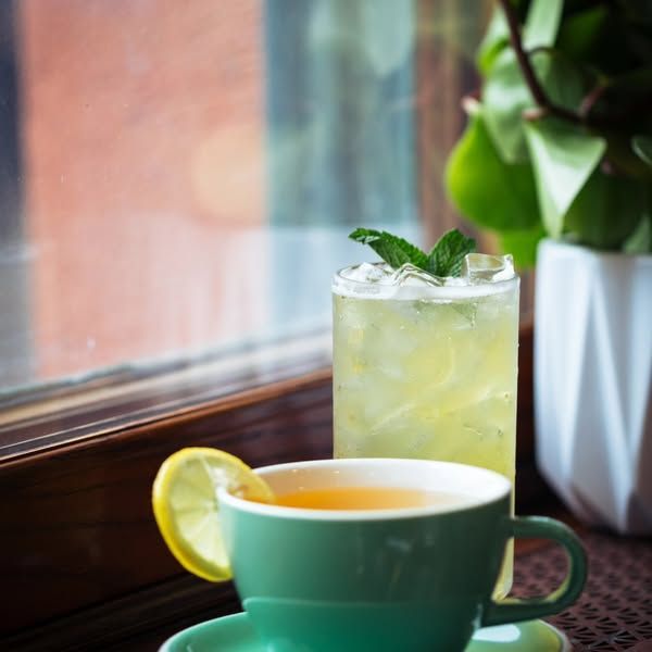 A green cup of tea sits next to a glass of lemonade