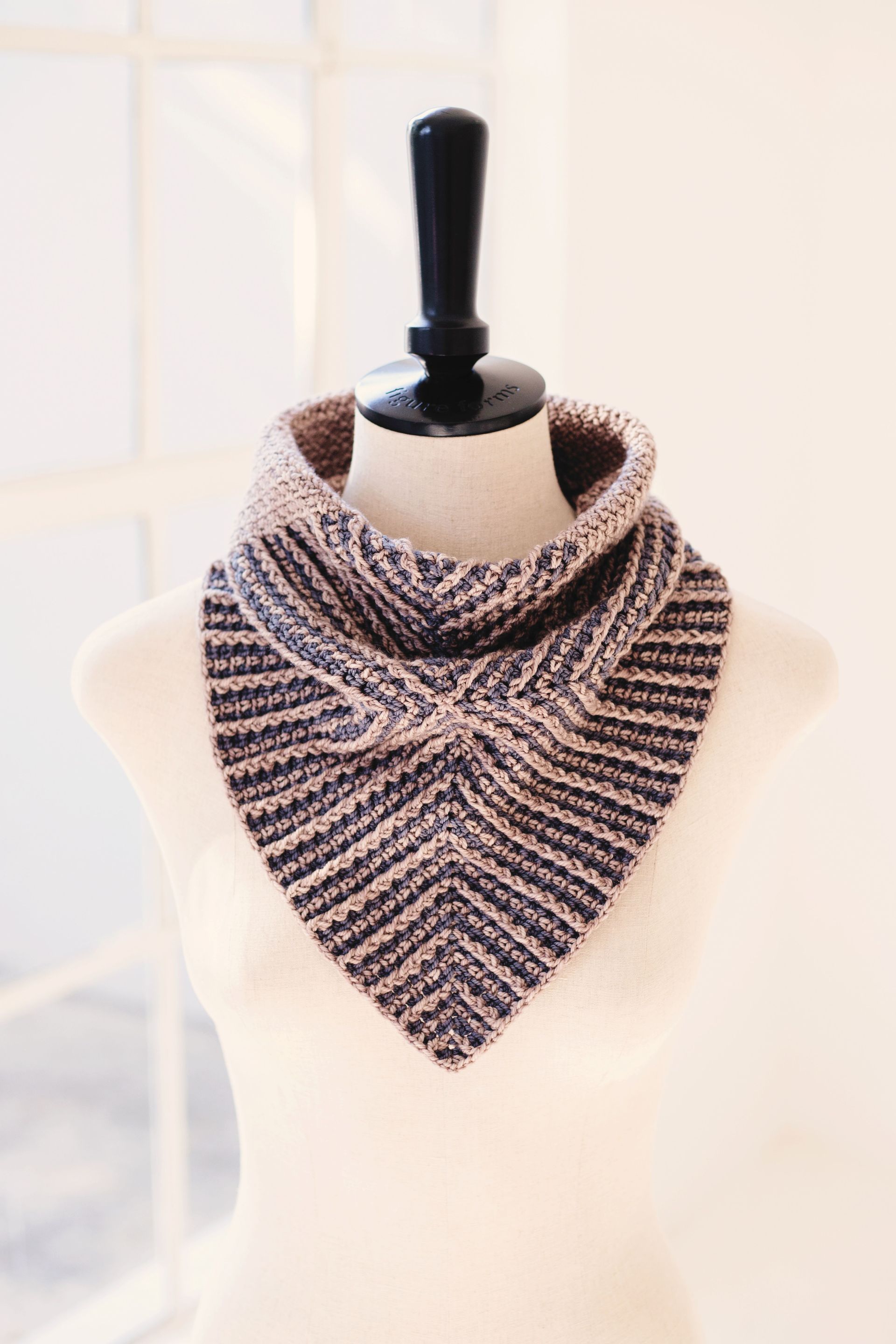 Crocheted cowl scarf on a mannequin, two-toned brown and black, triangular shape with a folded collar.