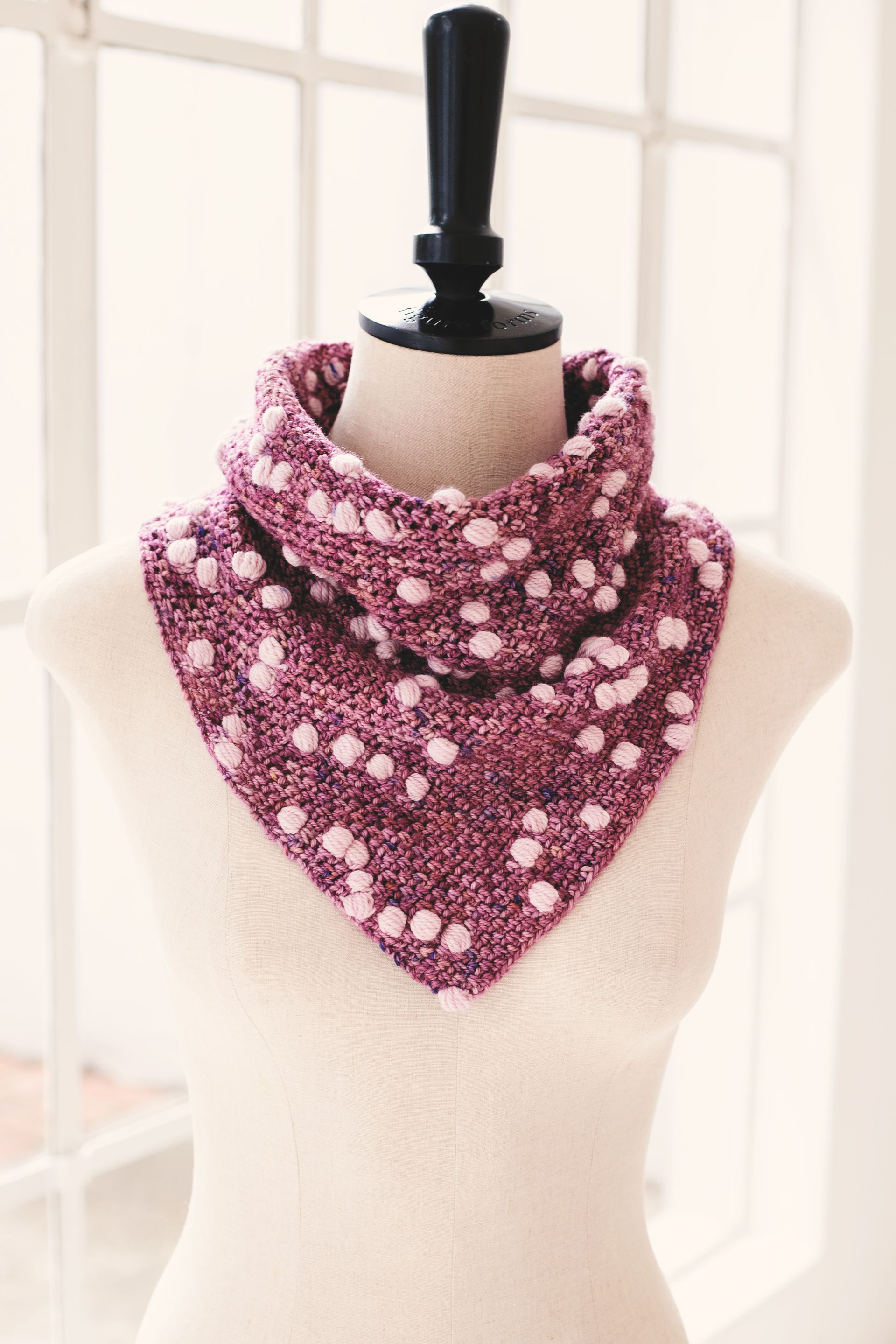 Pink crocheted triangular scarf with white bobbles on a dress form mannequin
