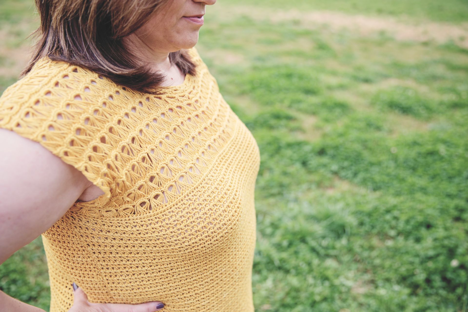 Woman in mustard yellow knit top outdoors, with openwork shoulder detailing.