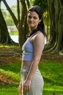 Woman in light blue crop top and beige pants poses outdoors in front of trees.
