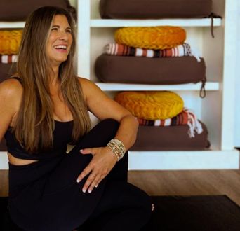 Woman in black activewear smiles while doing yoga; shelves with cushions in the background.