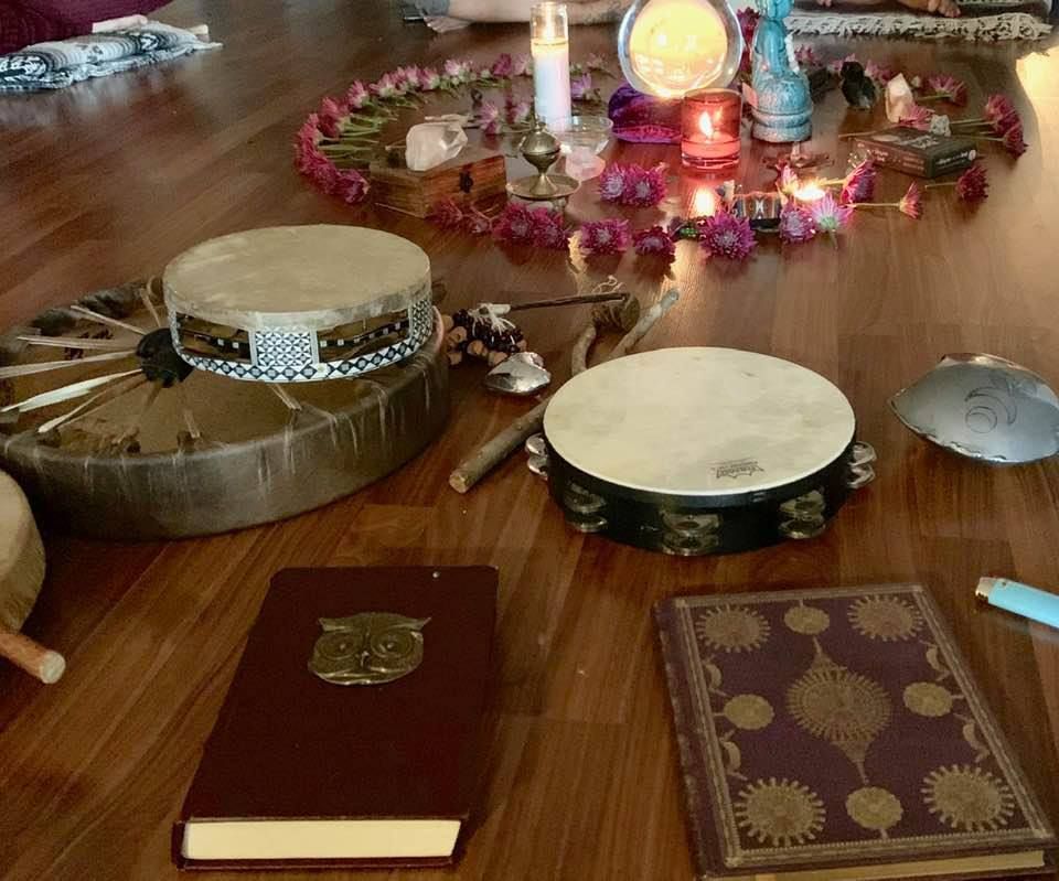 Wooden floor with drums, books, candles, and a floral arrangement; spiritual setting.