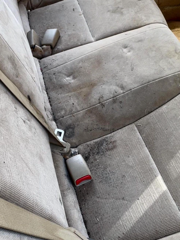 A dirty car seat with a seat belt on it.
