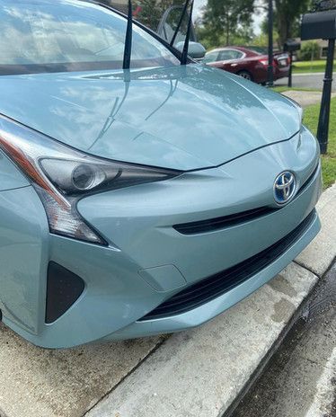 A blue toyota prius is parked on a sidewalk next to a mailbox.