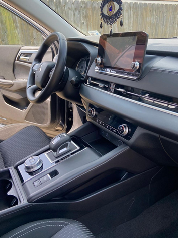The interior of a car with a steering wheel and a screen.