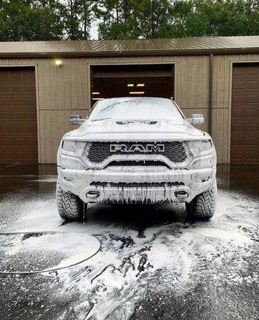 A white ram truck is covered in foam in front of a garage.