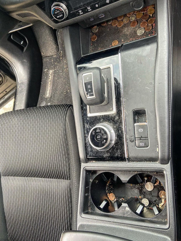 A dirty car console with a lot of coins in it.