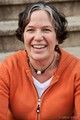 A woman in an orange sweater is smiling for the camera.