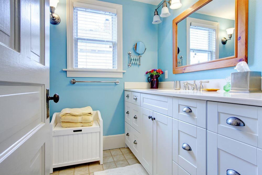 A Bathroom With Blue Walls and White Cabinets and a Large Mirror — Knobel Builders In Dapto, NSW