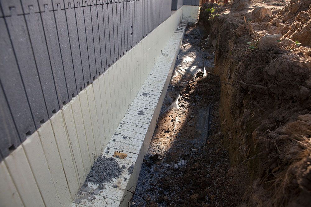A Drainage System is Being Installed on the Side of a Building — Knobel Builders In Austinmer, NSW