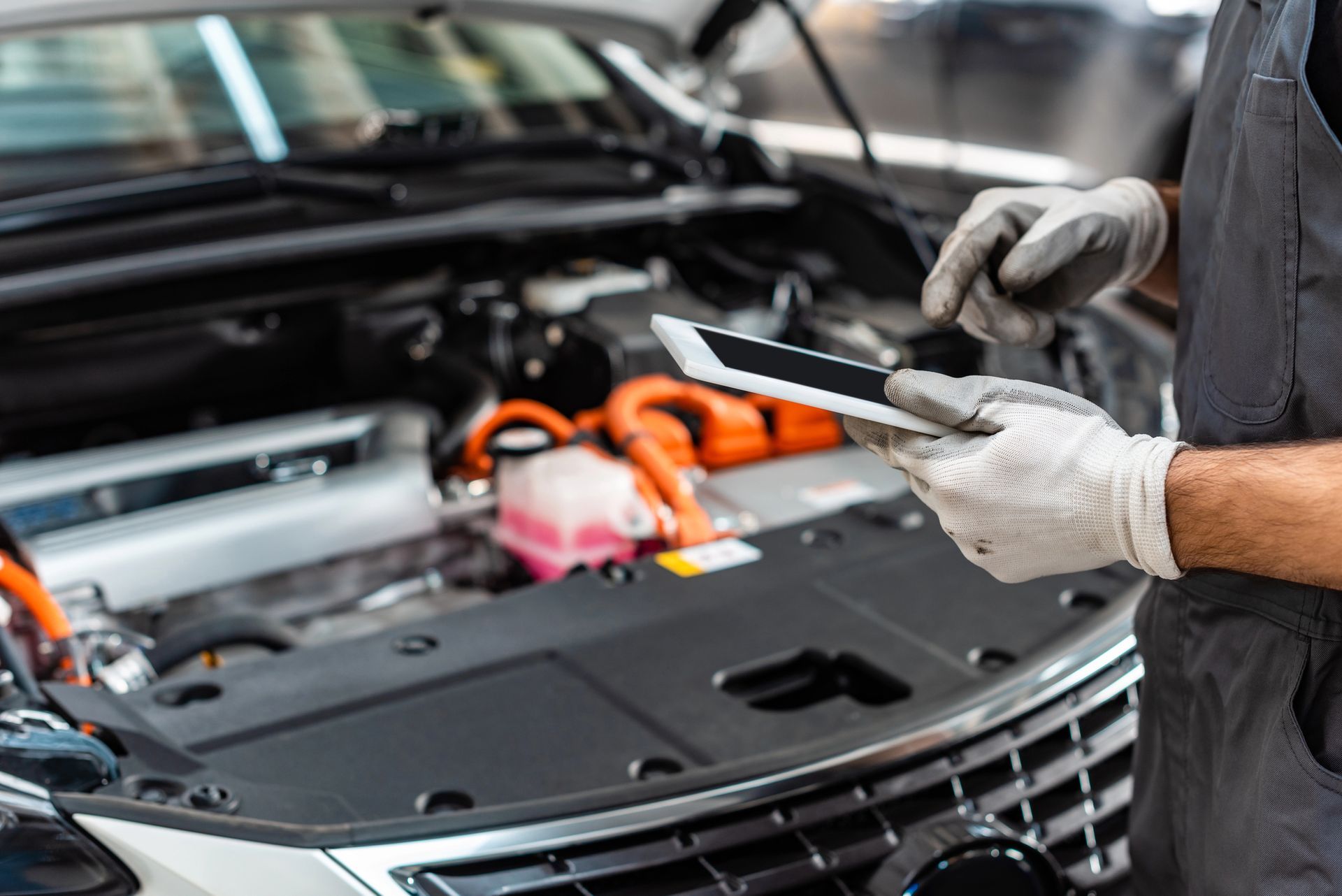 Un meccanico con i guanti controlla il vano motore di un'auto con uno strumento diagnostico.