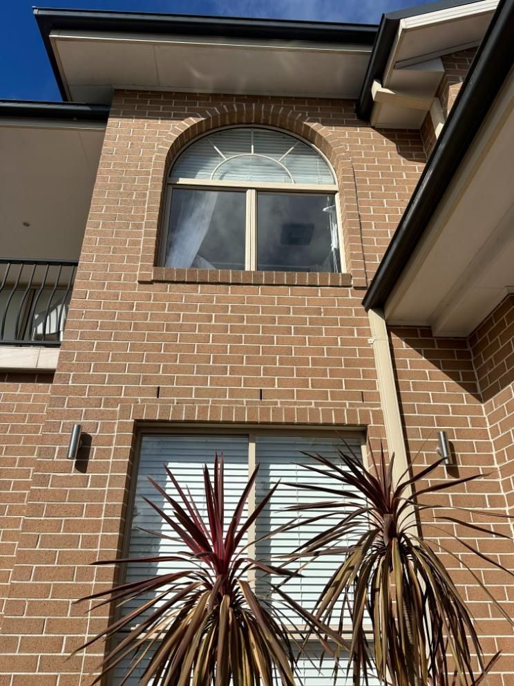 A Brick Building With A Window And A Palm Tree In Front Of It — Central Coast Glass & Glazing In Gosford, NSW